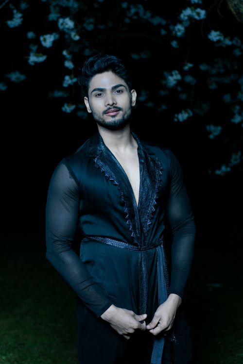 Free Portrait of a fashionable man wearing stylish black attire under night sky with floral backdrop. Stock Photo