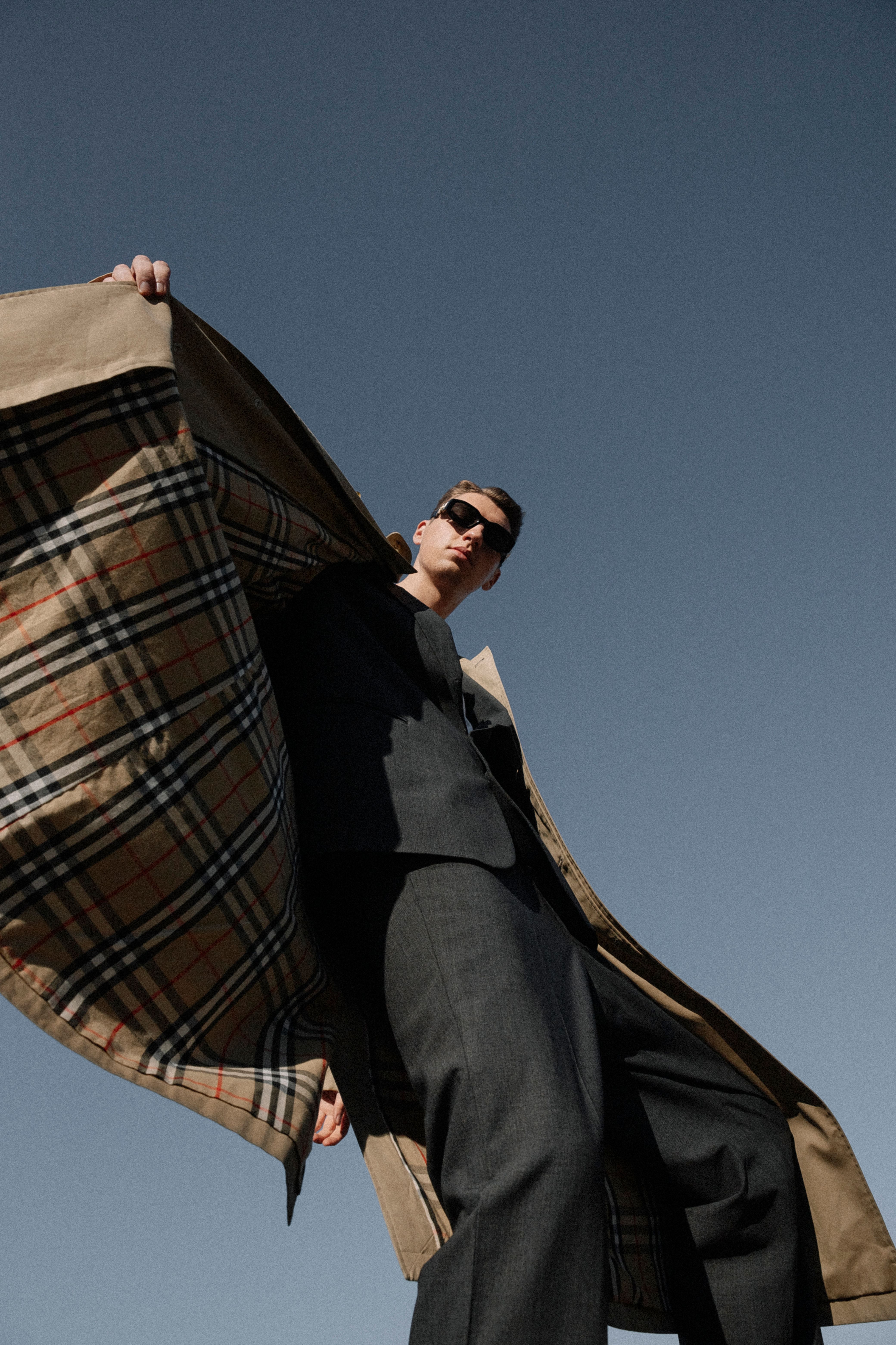 Low angle shot of a fashionable man in sunglasses displaying coat lining outdoors.