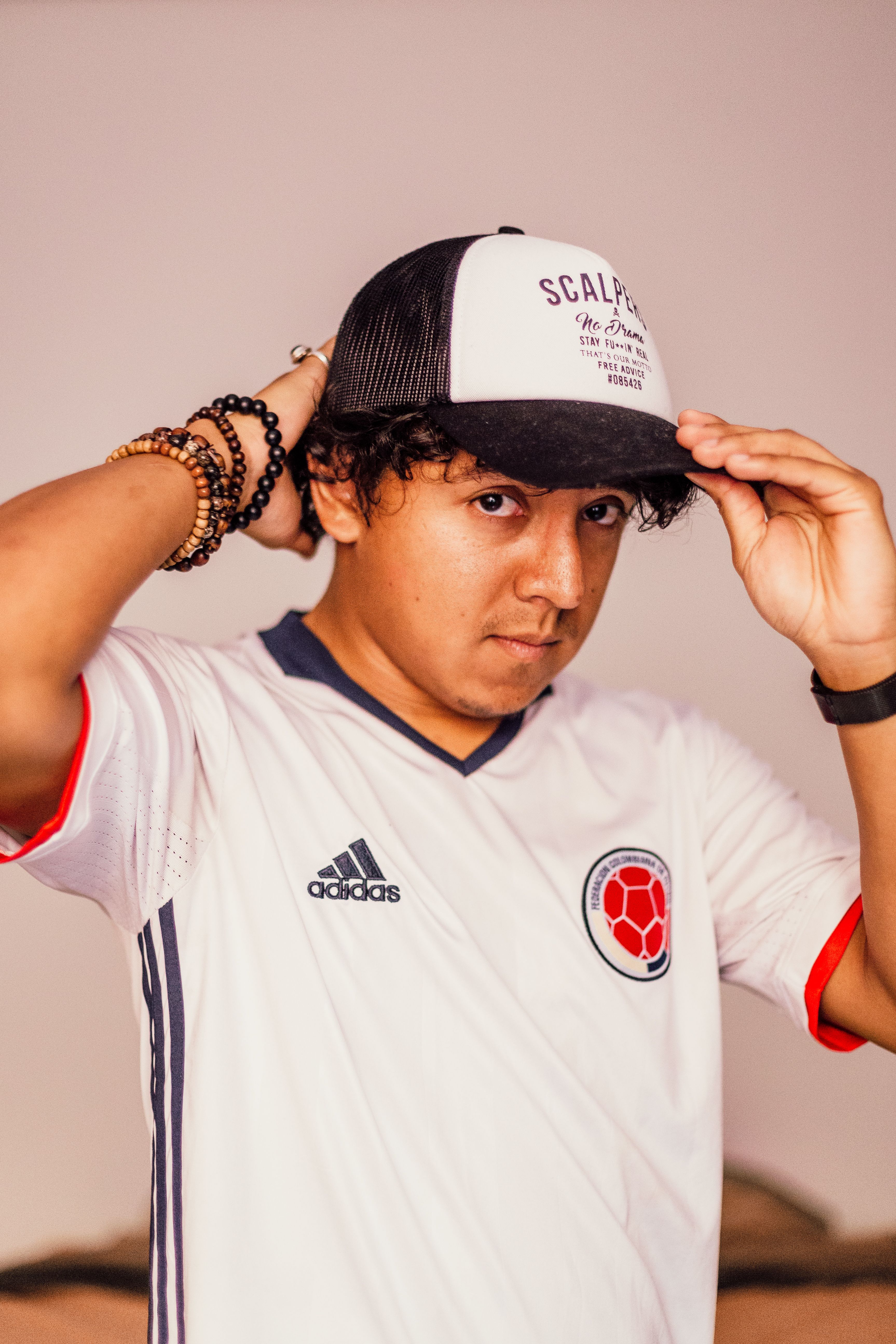 Young man wearing a sports jersey and cap, posing indoors with casual style and accessories.