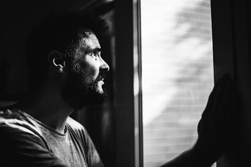 Greyscale Photo of Man Looking Through Window
