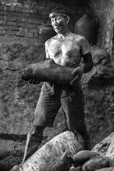 A hardworking miner covered in soot carries a heavy log in an underground setting.