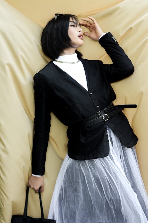 A Woman in Black Jacket and White Skirt Standing Beside Beige Fabric