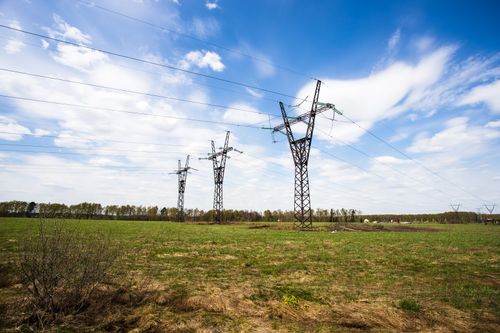 Free Scenic view of power lines crossing a green field under a bright blue sky. Stock Photo