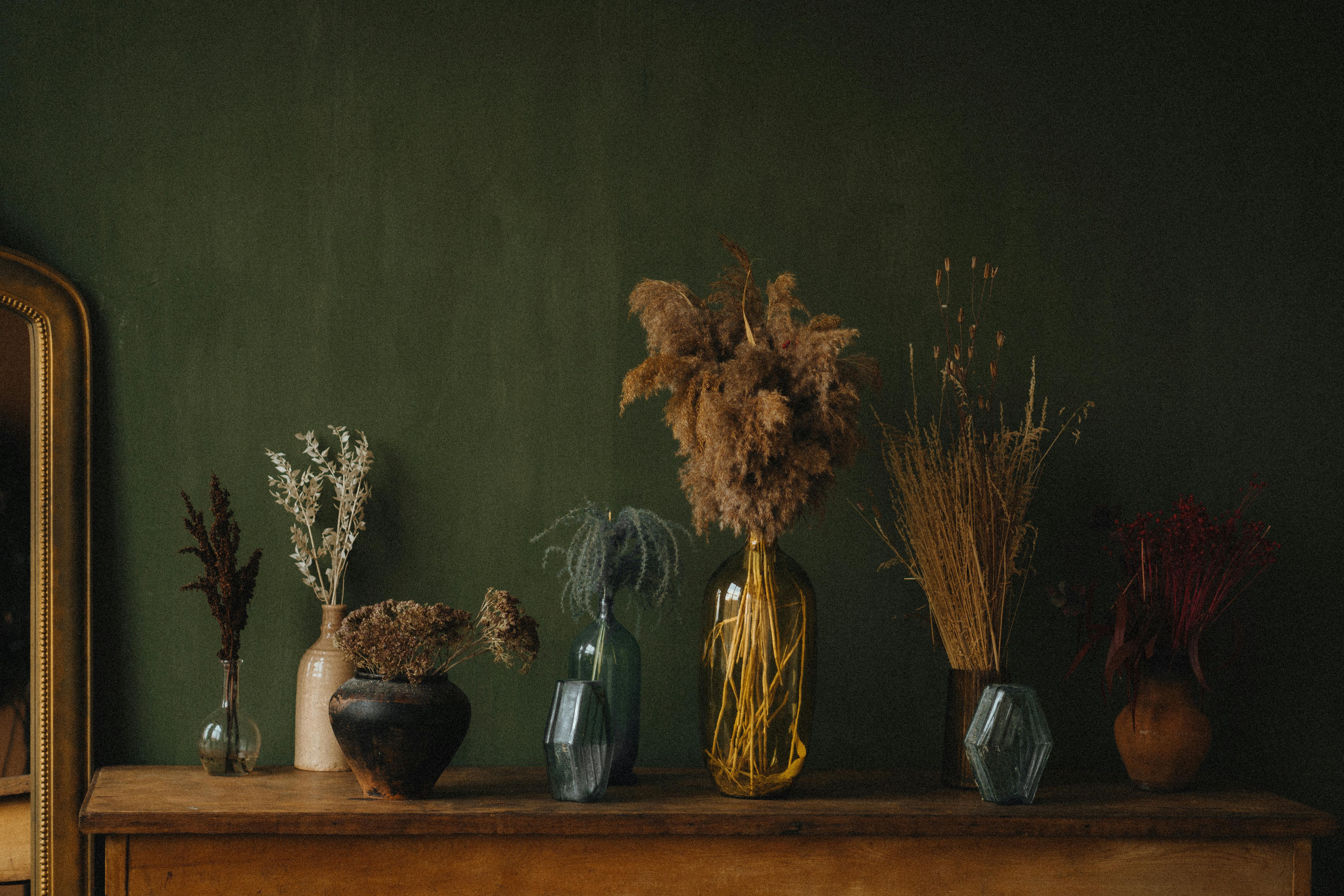 Stylish still life showcasing diverse dried plants in various vases on a wooden table.