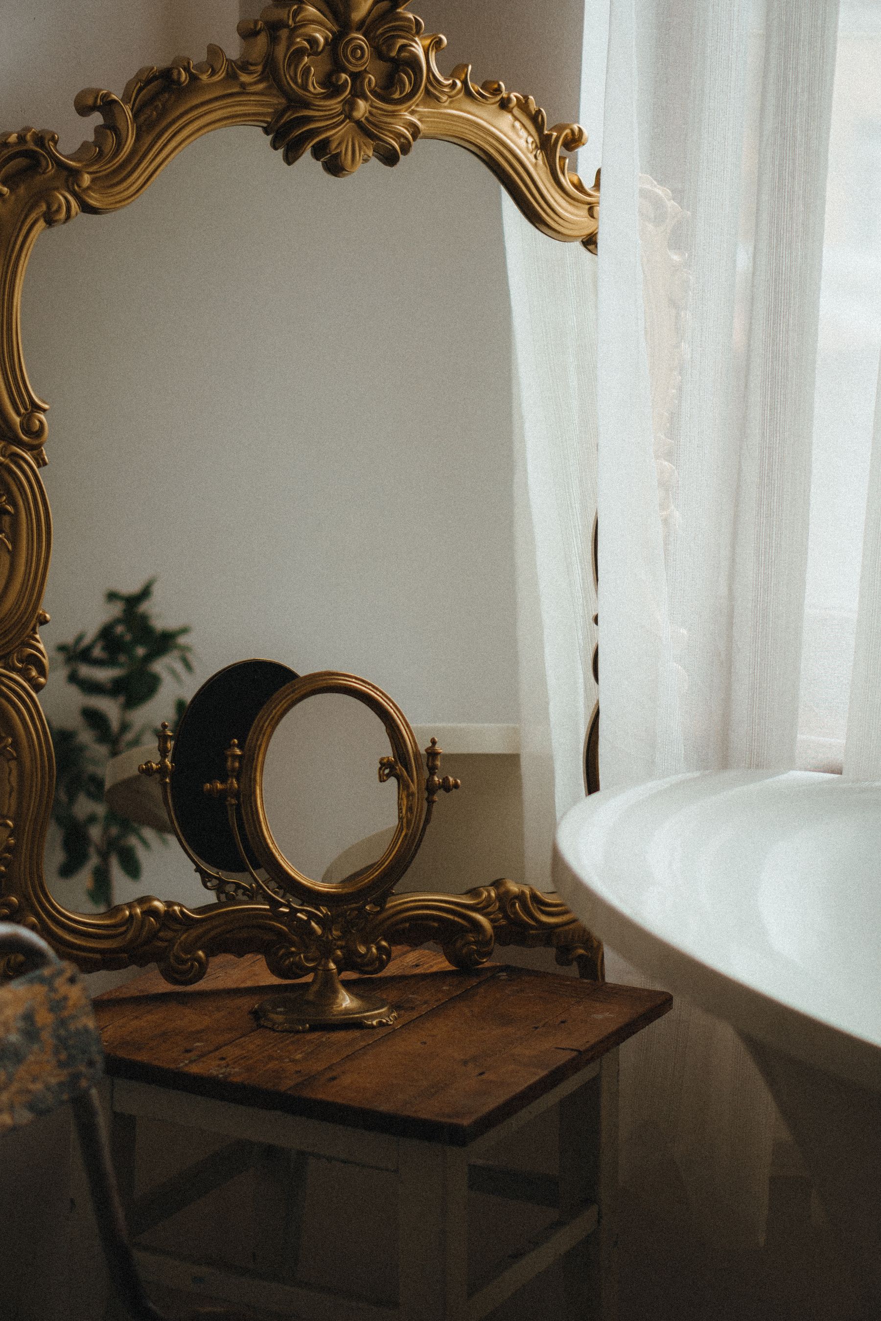 Classic bathroom with ornate gold mirror beside a clawfoot bathtub
