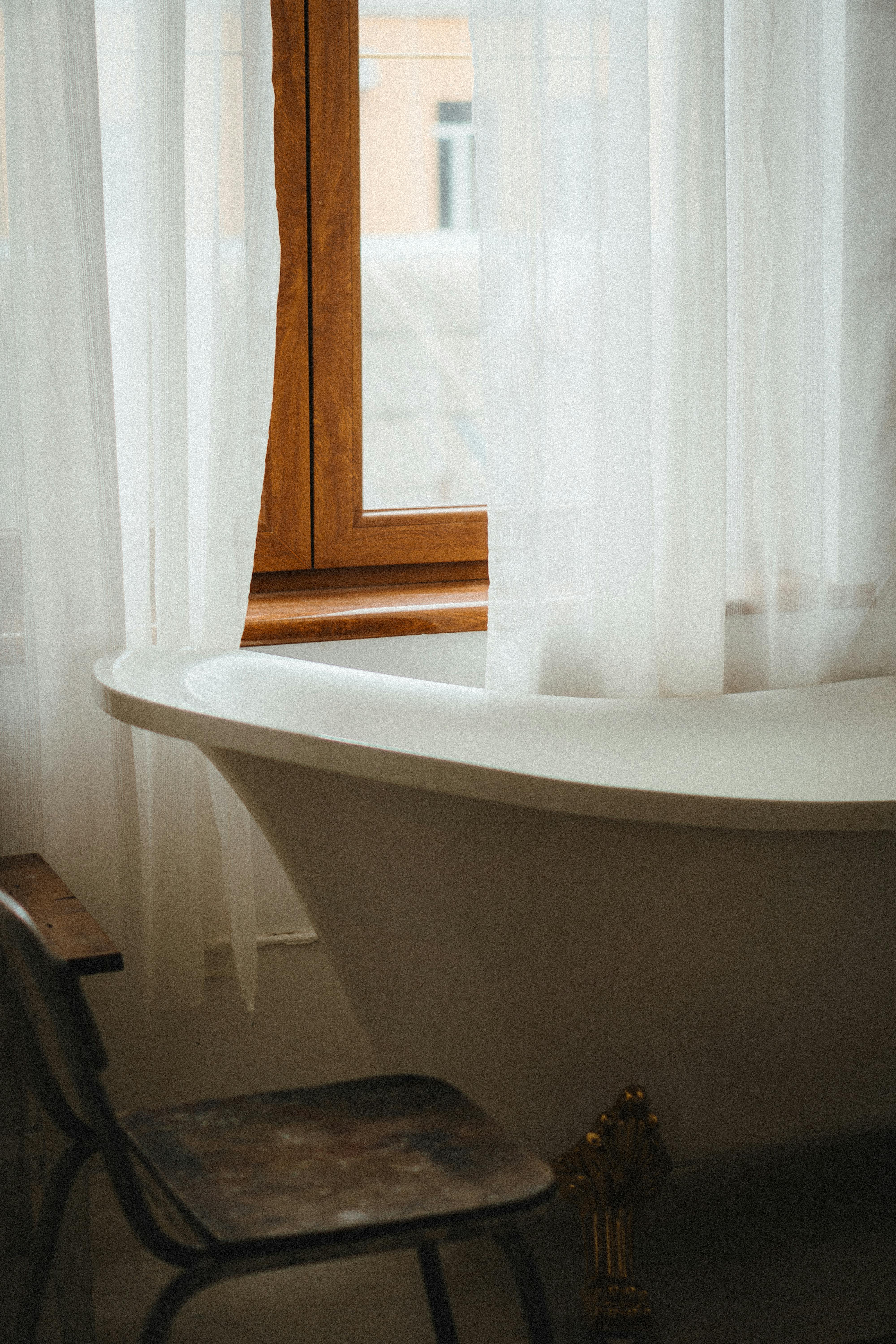 Vintage-style bathroom featuring a clawfoot bathtub, wooden window, and soft curtains. Ideal for decor inspiration.