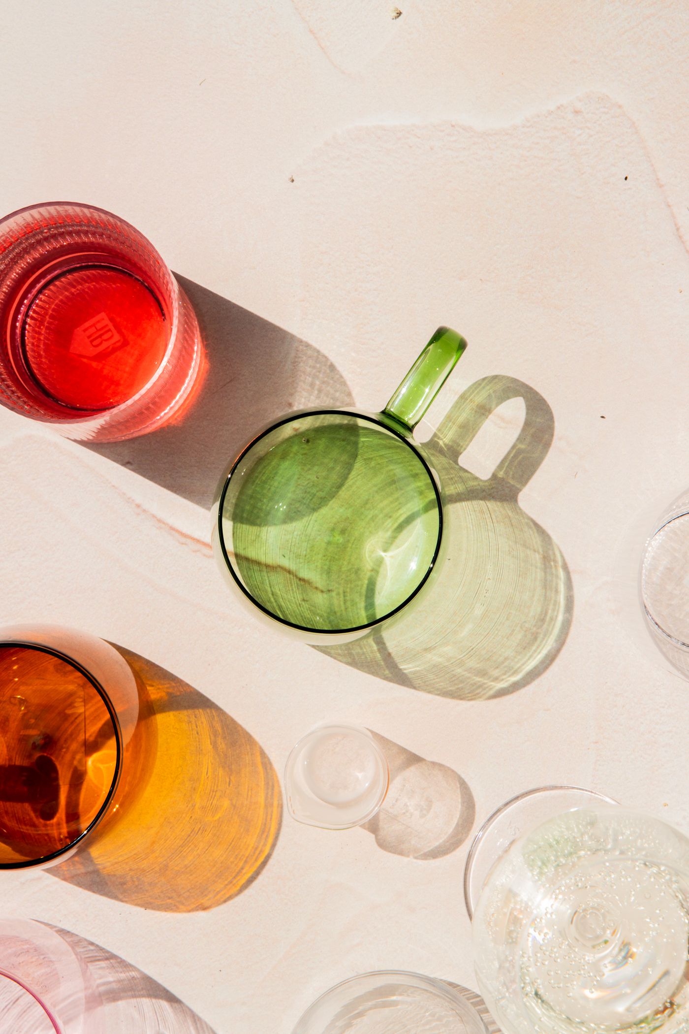 Colored drinking glasses arranged in sunlight with transparent reflections and shadows