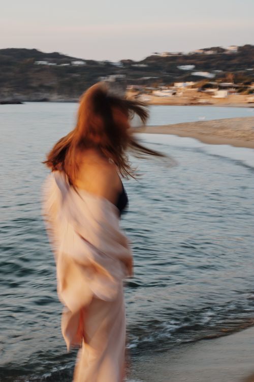 Free A woman in motion captured at a seaside during sunset, evoking a sense of freedom. Stock Photo
