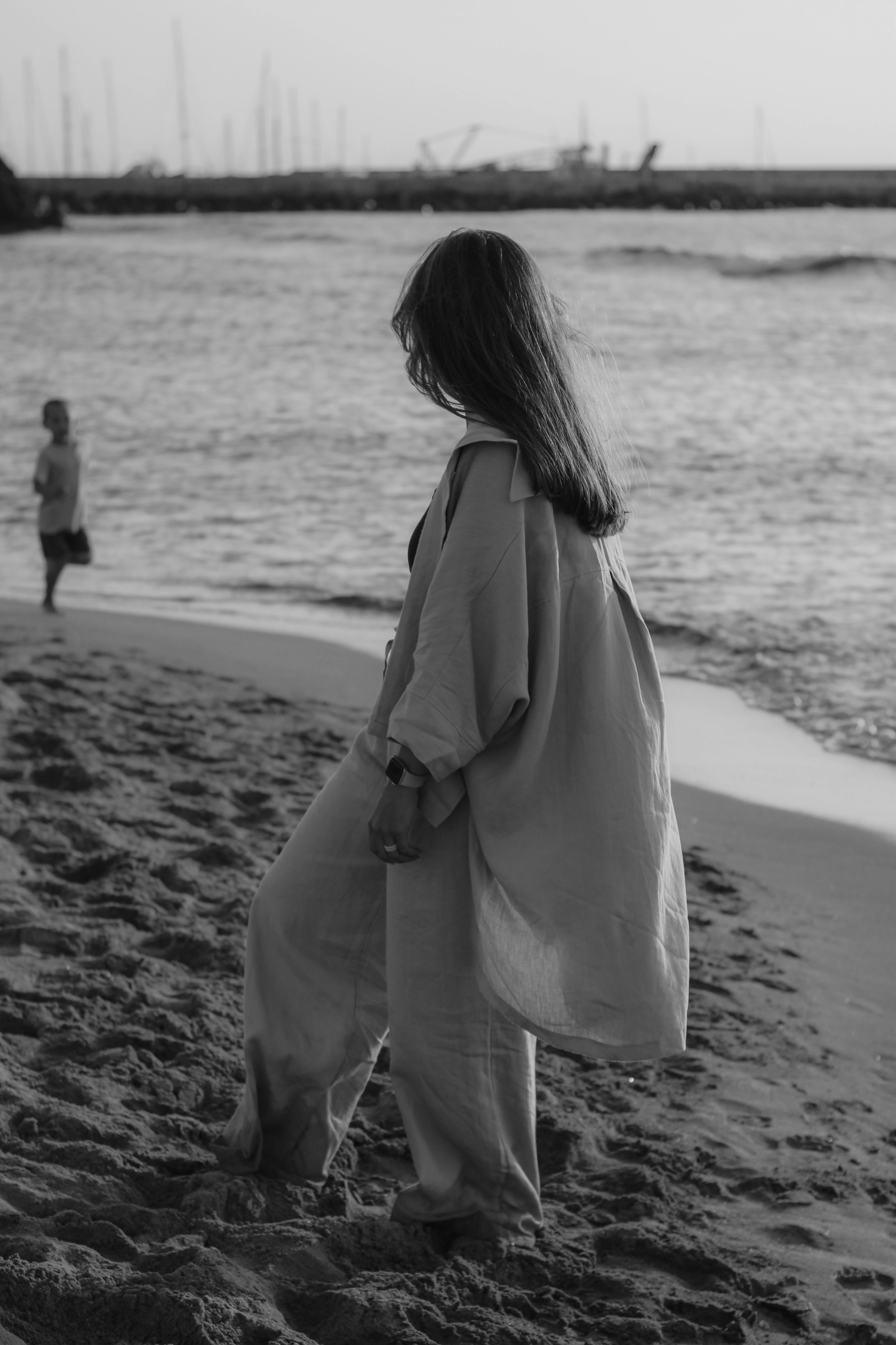 A contemplative woman walks along the beach, captured in black and white for a timeless feel.