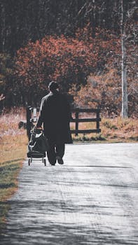 A man in a coat walks along a park path in Ottawa, Canada, pulling a trolley bag outdoors on a crisp fall day.