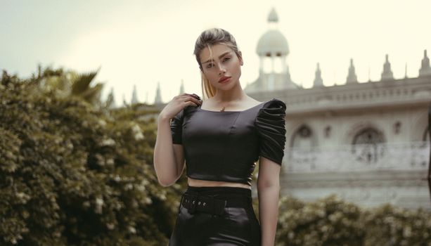 Fashion portrait of an elegant woman in a trendy crop top posing outdoors against architectural backdrop.