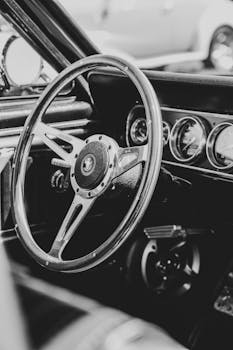 Monochrome close-up of a classic car interior showcasing steering wheel and dials.