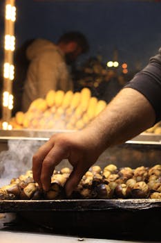 Close-up of a hand picking roasted chestnuts from a tray at a night market.