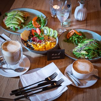 Colorful brunch with avocado toast, fruit bowl, latte art, and cappuccino on a wooden table.
