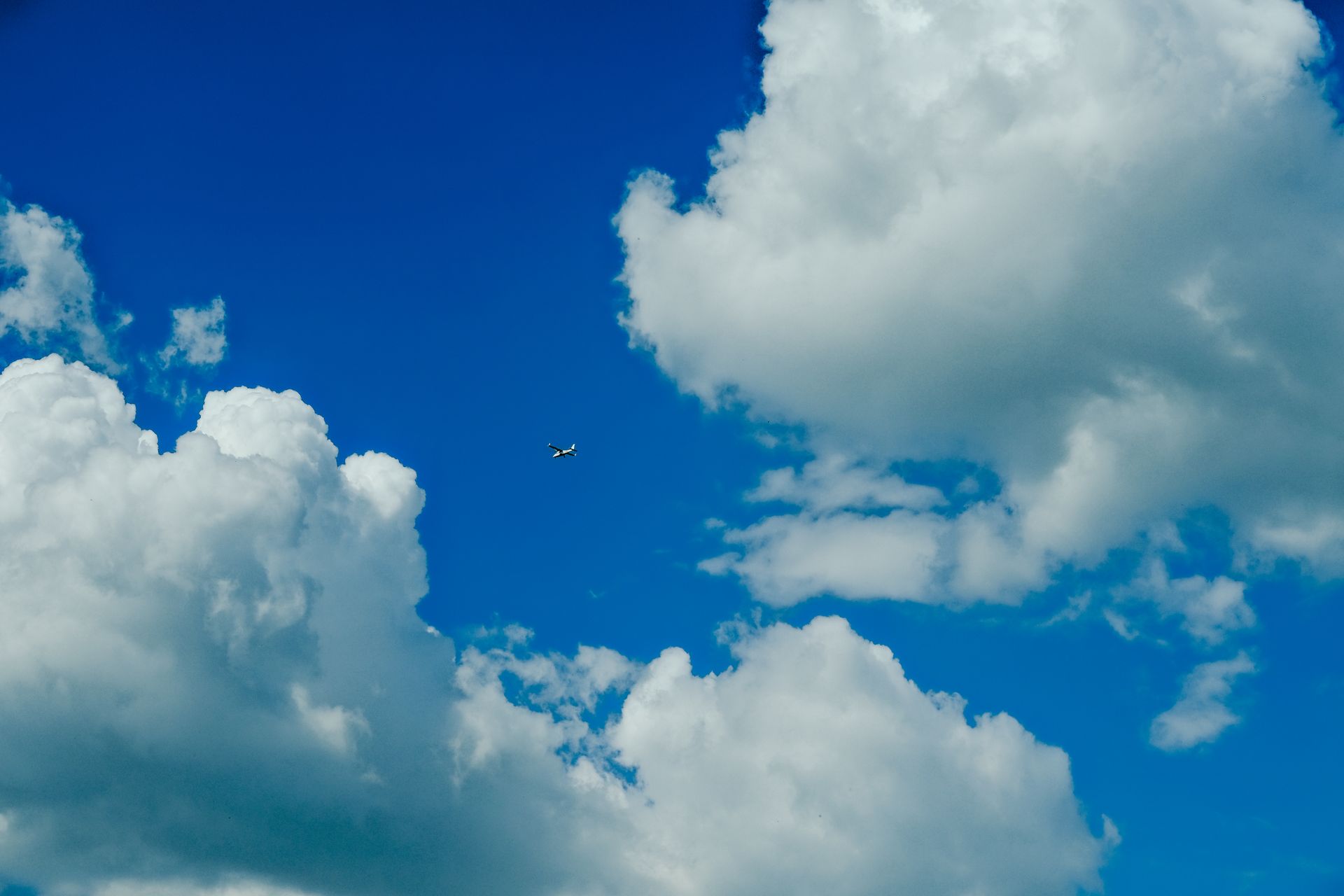 Small airplane flying high in a clear blue sky surrounded by fluffy white clouds.