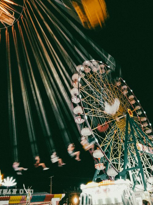 Free A vibrant nighttime scene at a fairground with a ferris wheel in motion, located in Ayvalık, Turkey. Stock Photo