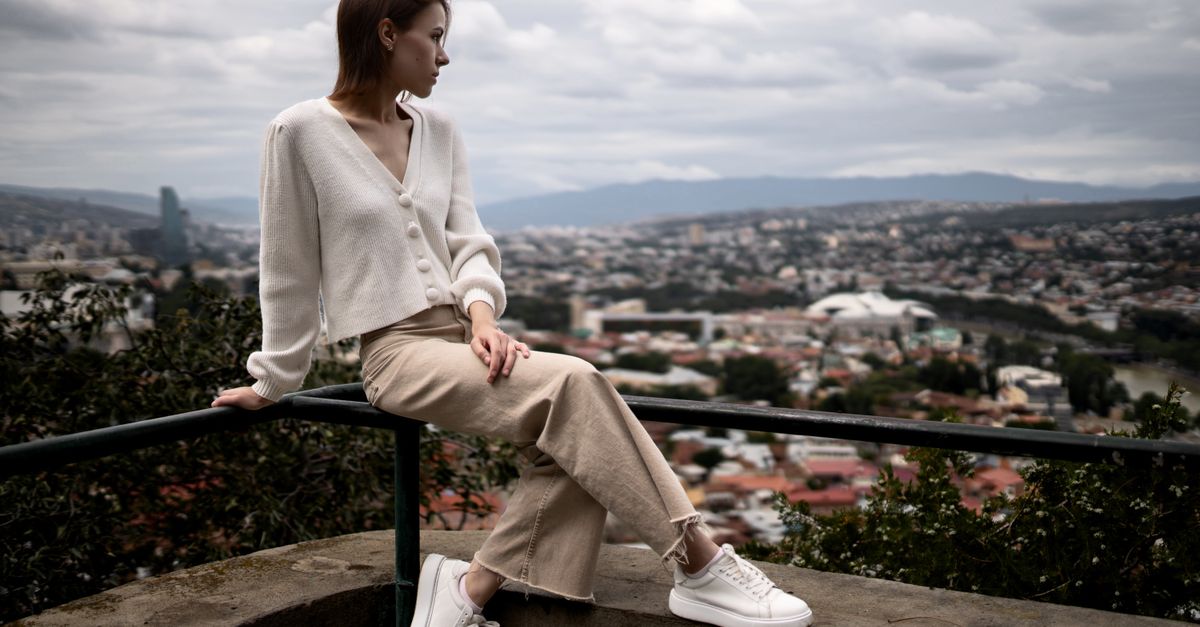 Woman sitting on a rail with city view, wearing casual outfit, serene expression.