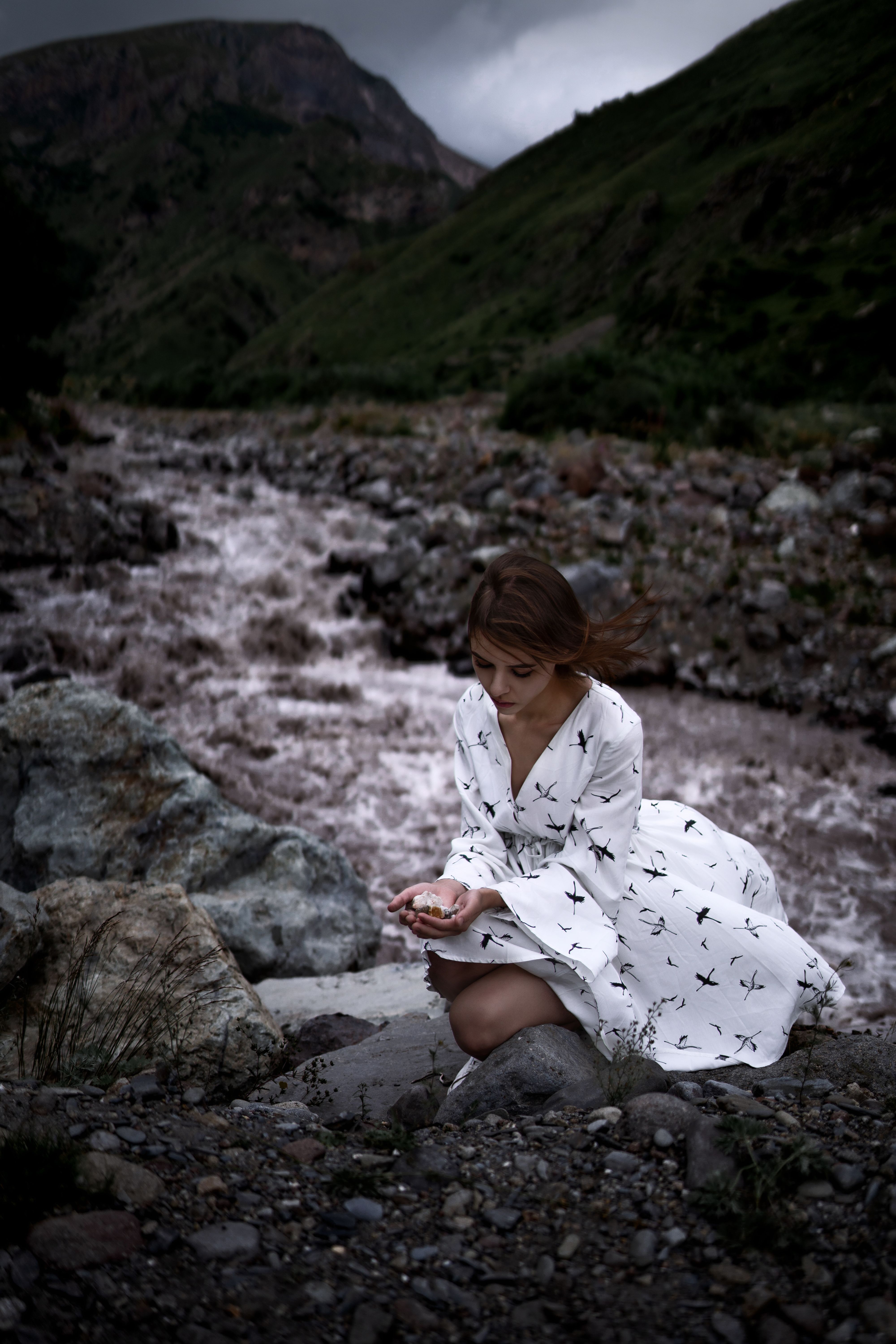 A Woman in White Dress Sitting while Looking at the Rock She is Holding ...