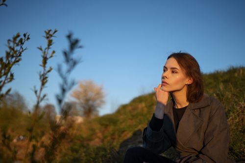 Free A thoughtful young woman sits outdoors, enjoying the sunlight and contemplating nature. Stock Photo