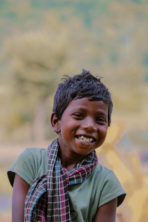 Free A cheerful young boy wearing a scarf smiles brightly in a natural setting. Outdoor portrait. Stock Photo