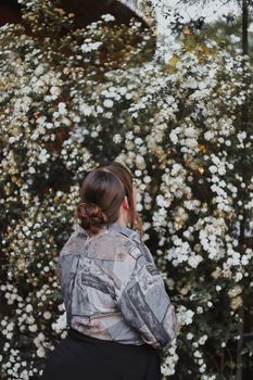 A woman in a patterned jacket stands outdoors, admiring a wall of blooming white flowers in Berlin.