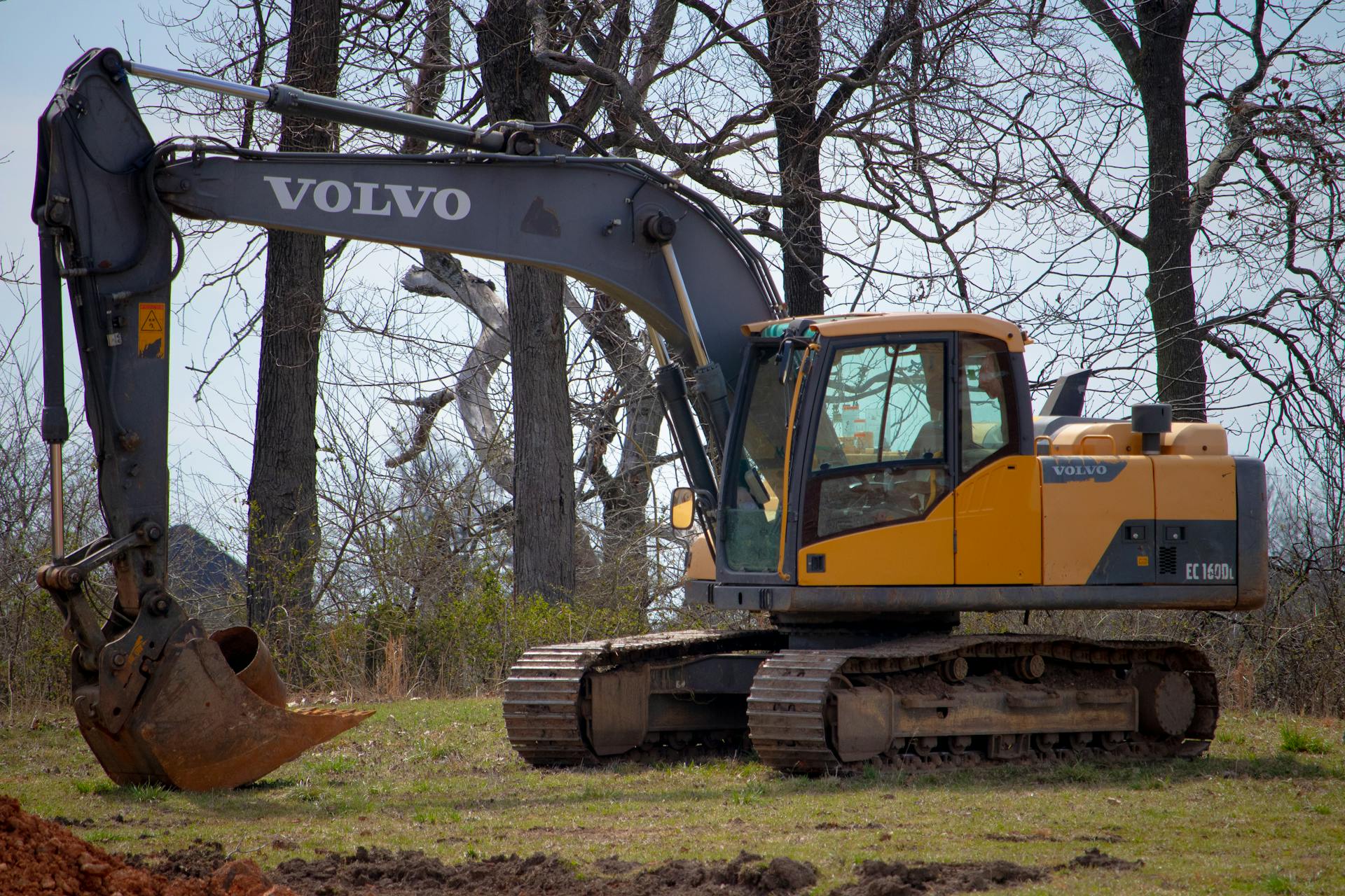 A yellow excavator in a field with leafless trees, showcasing construction equipment in nature.