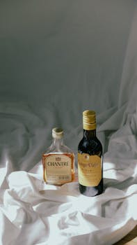 An artistic display of two liquor bottles on draped fabric, illuminated by soft light.