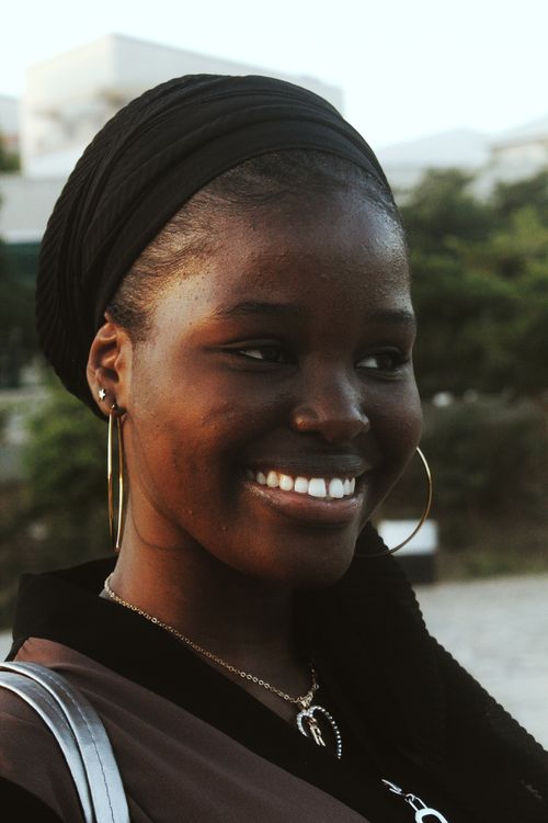 Free Close-up portrait of a smiling woman wearing a black headscarf and hoop earrings, outdoors in Abuja. Stock Photo