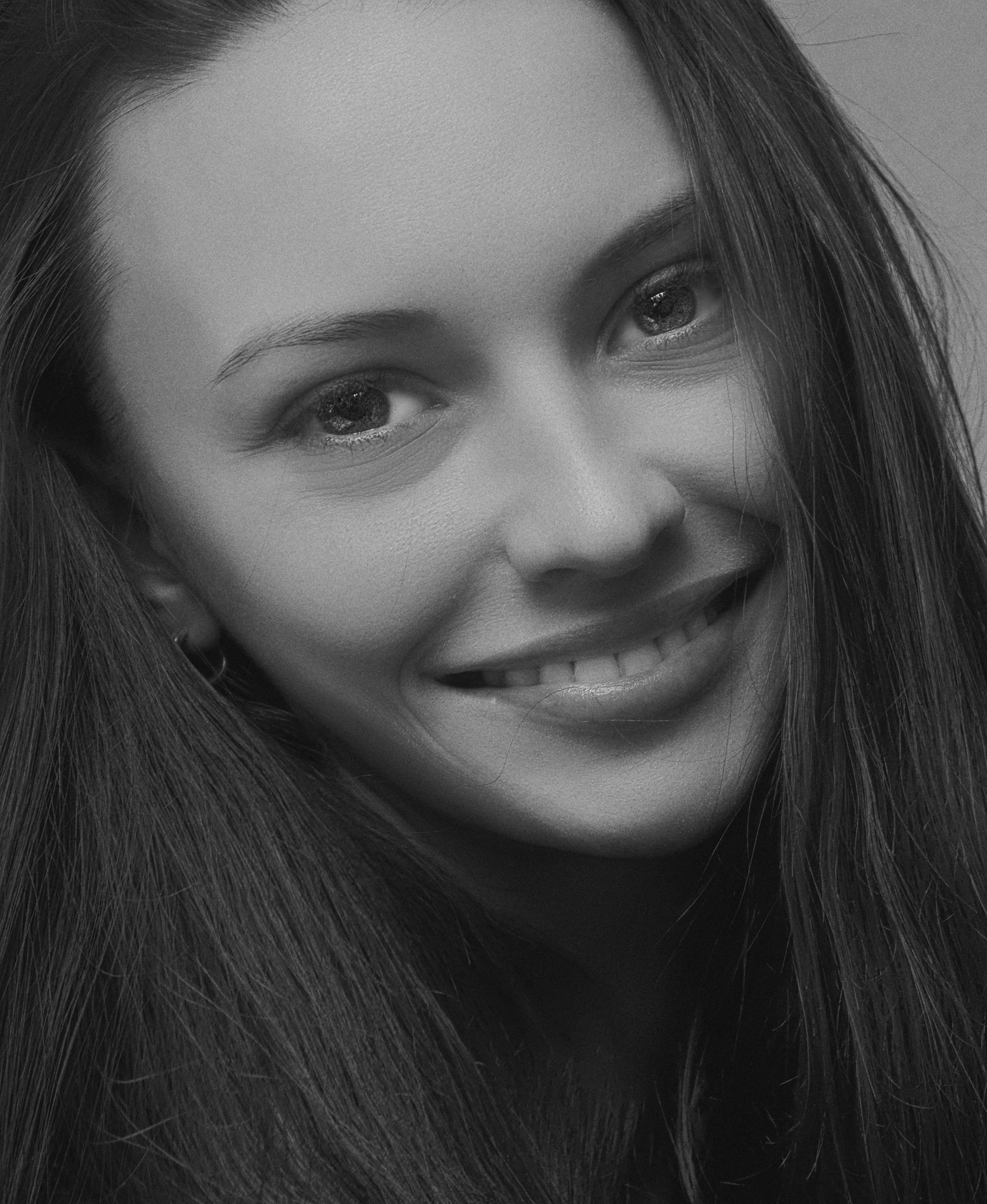 Close-up black and white portrait of a smiling woman with long hair, showcasing elegance and natural beauty.