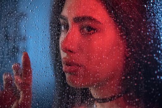Woman looking through a wet window, moody lighting in Tehran, Iran.
