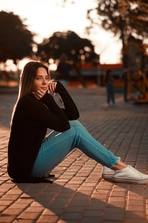 Woman in Black Long Sleeve Shirt and Blue Denim Jeans Sitting on the Street