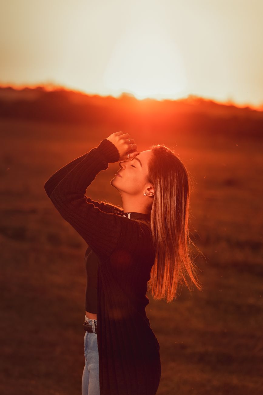 A young woman enjoys the warm glow of sunset outdoors, capturing serene moments in nature.