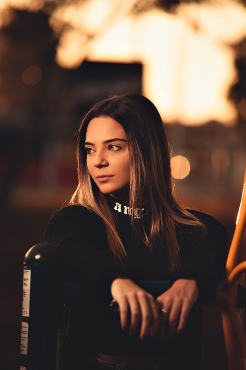 Free A thoughtful woman in a black turtleneck leans on a metal fence during sunset, capturing a serene and moody moment. Stock Photo