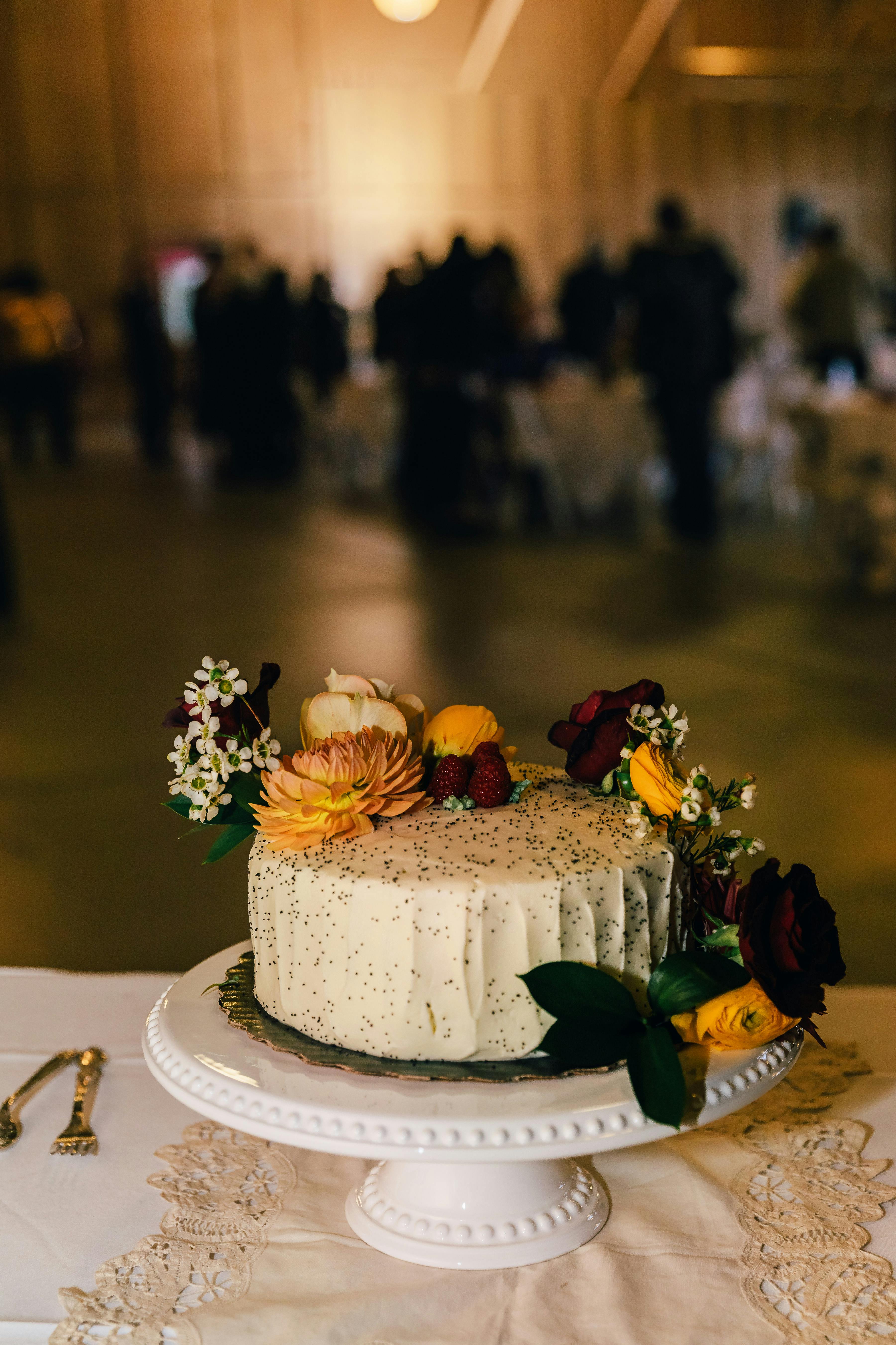 Close-up of a beautifully decorated floral wedding cake on a cake stand in an indoor reception setting.
