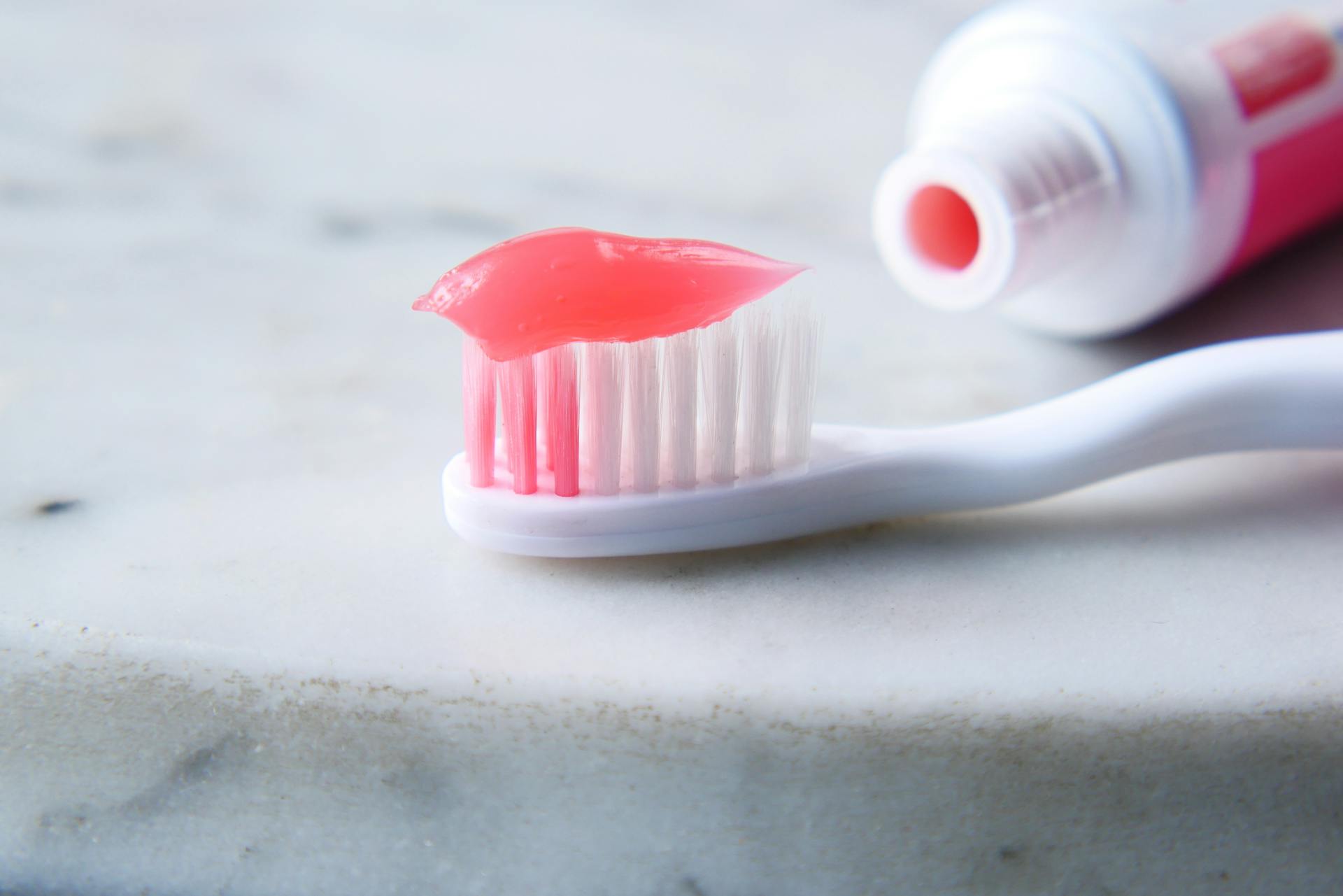 Close-up of a white toothbrush with red toothpaste against a white surface, highlighting dental care essentials.