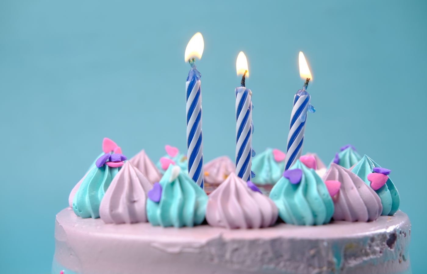 A vibrant birthday cake with pastel icing and lit candles, perfect for celebrations.