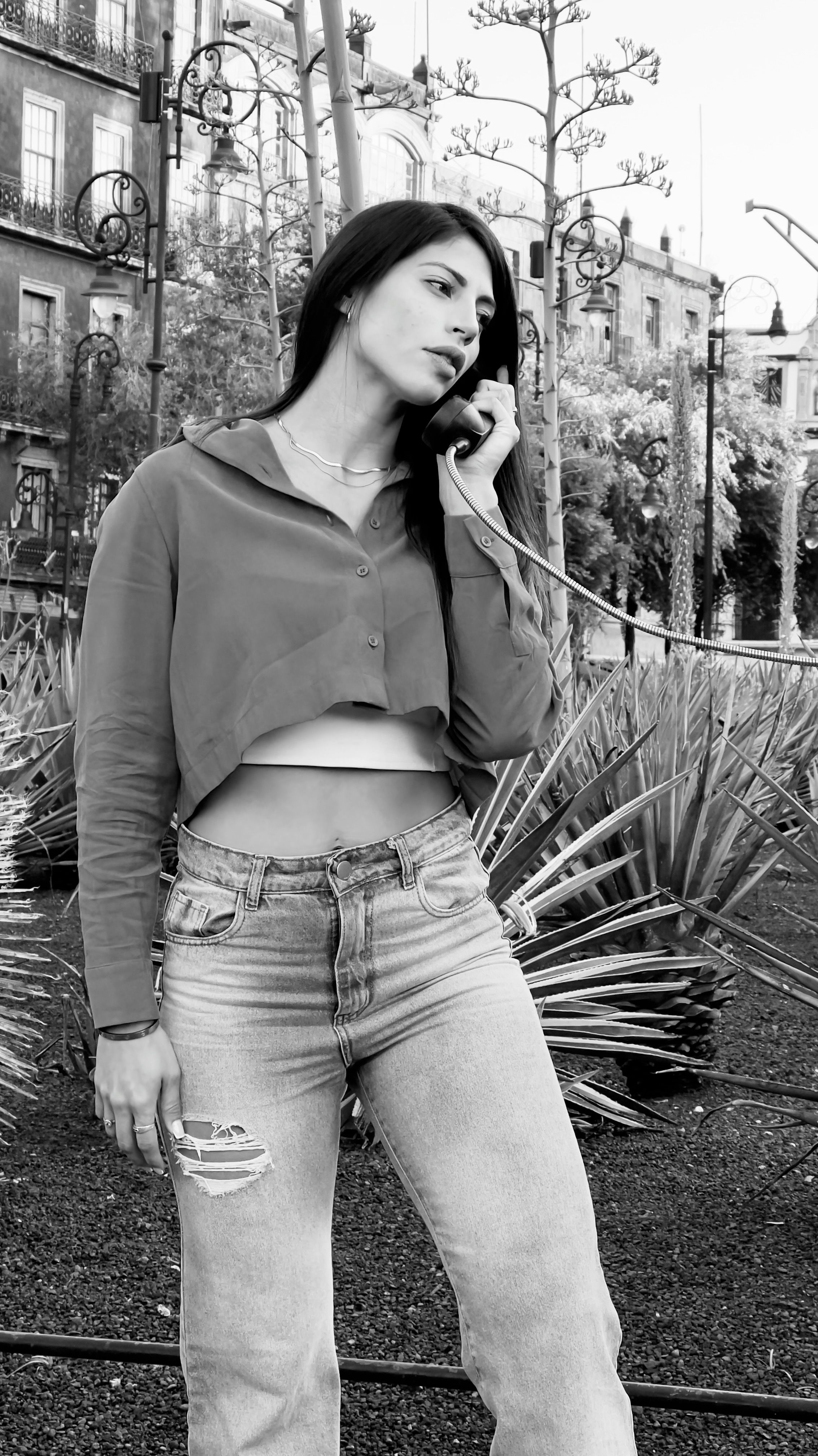 Black and white image of a woman in a crop top using a phone in an urban park setting.