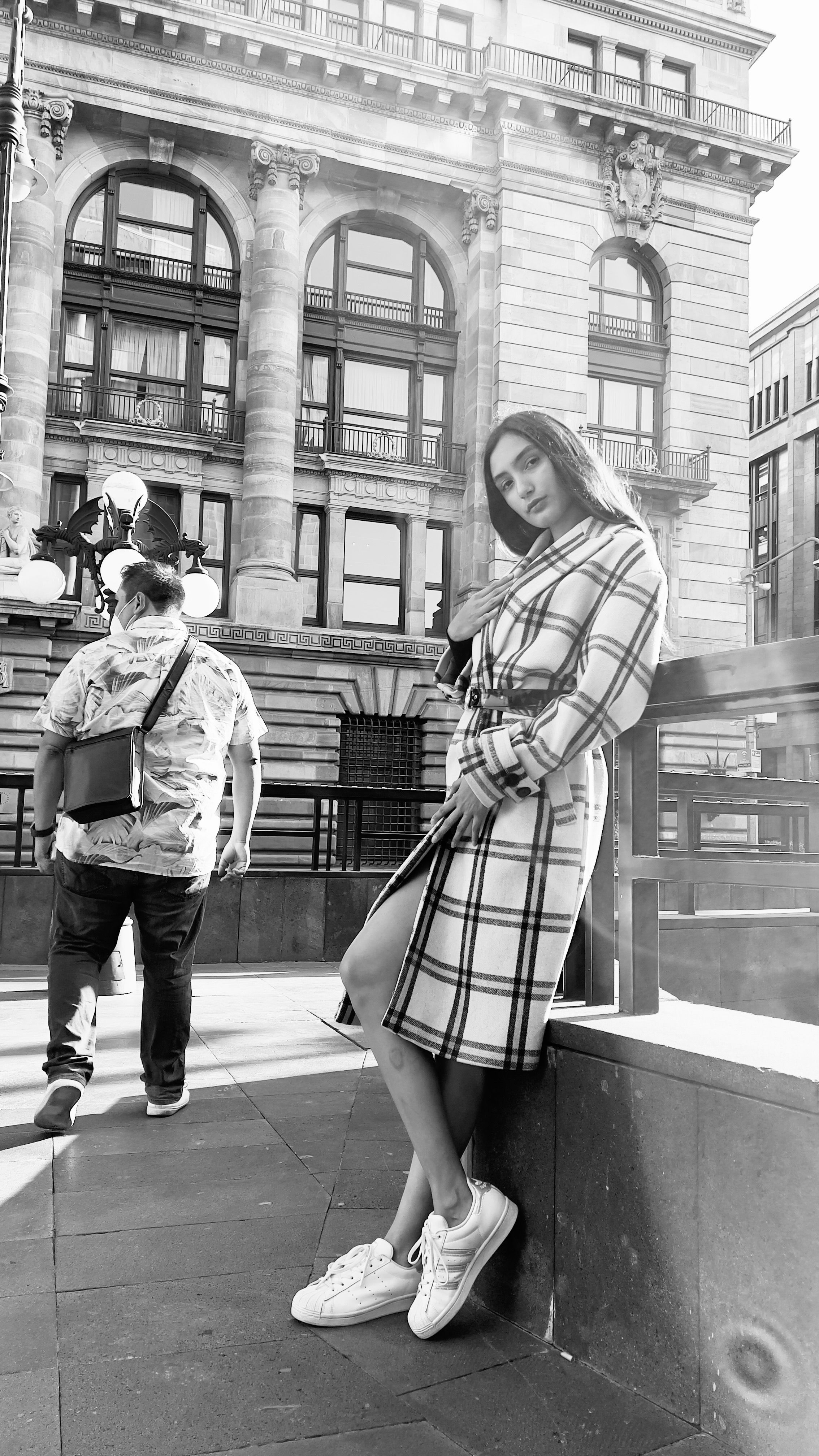 Stylish woman poses in a trendy plaid overcoat on a city street in black and white.