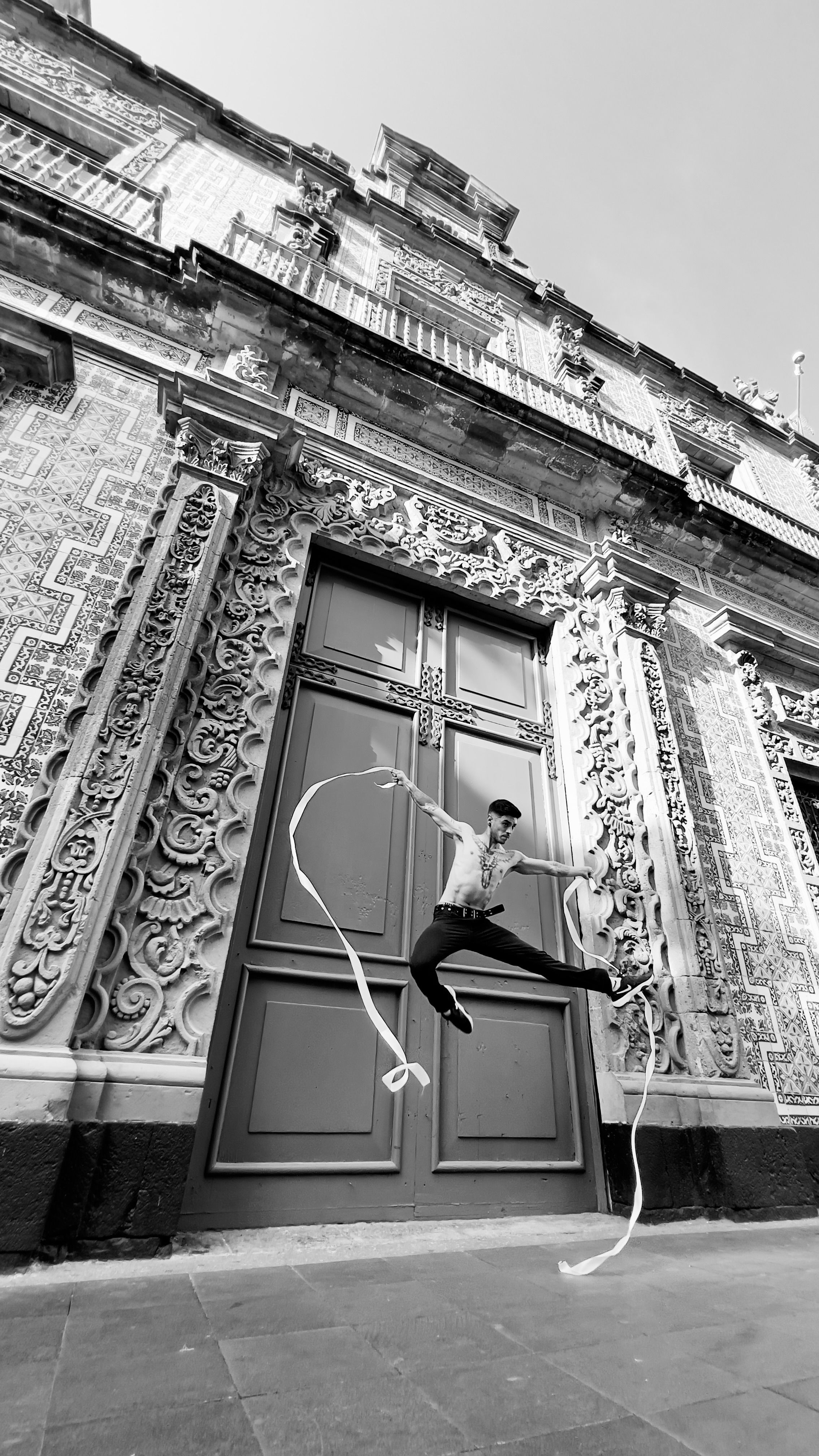 Graceful dancer captured midair in front of an ornate historic building facade.