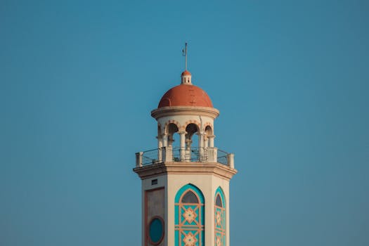 A beautifully detailed tower with a red dome set against a clear blue sky, showcasing architectural elegance.