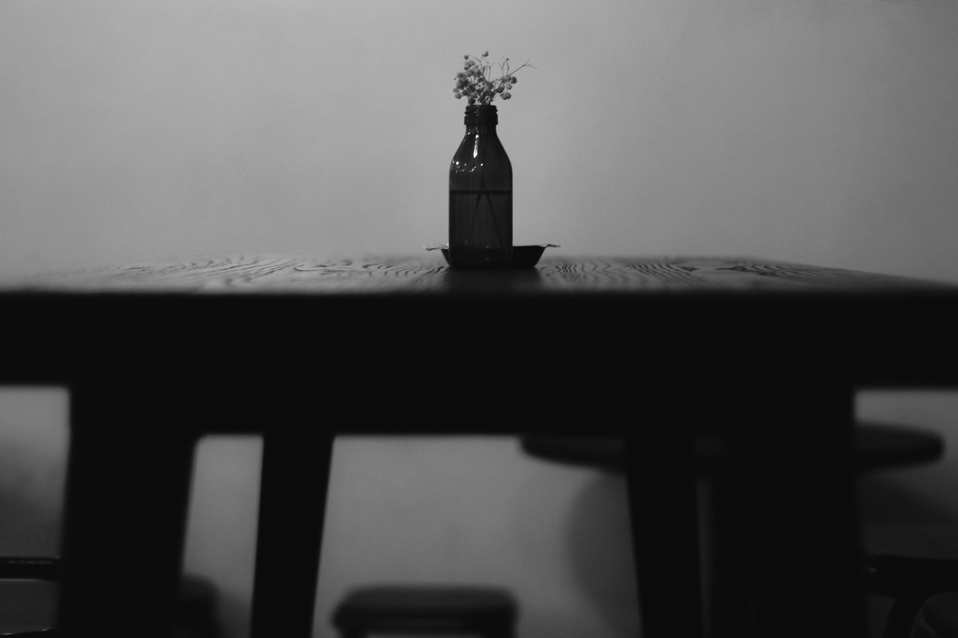 Una botella con unas flores secas sobre una mesa vacía