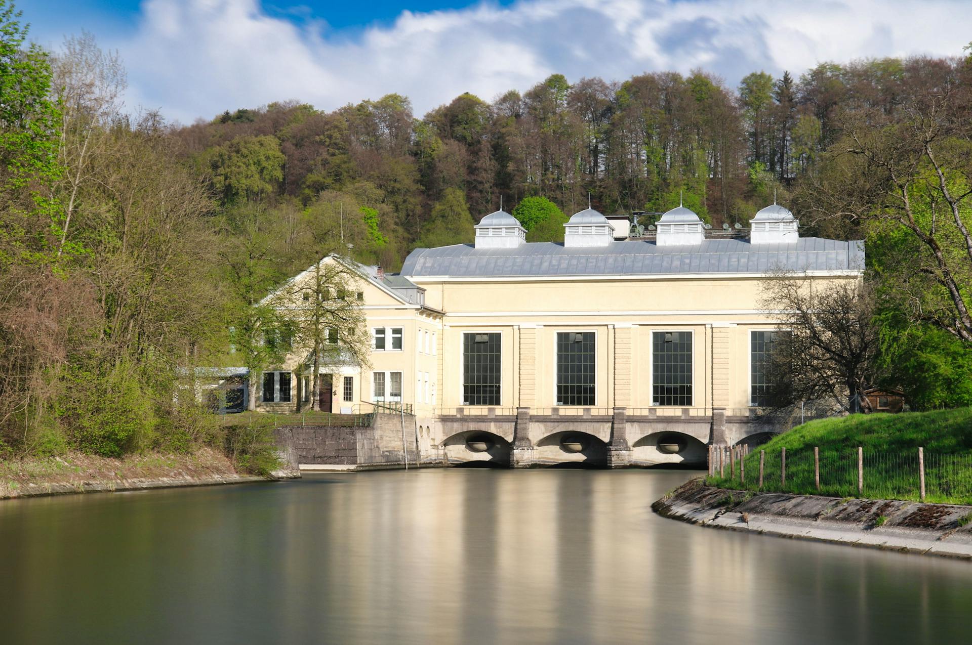 A picturesque hydroelectric power plant nestled by a serene river in a lush, wooded area.