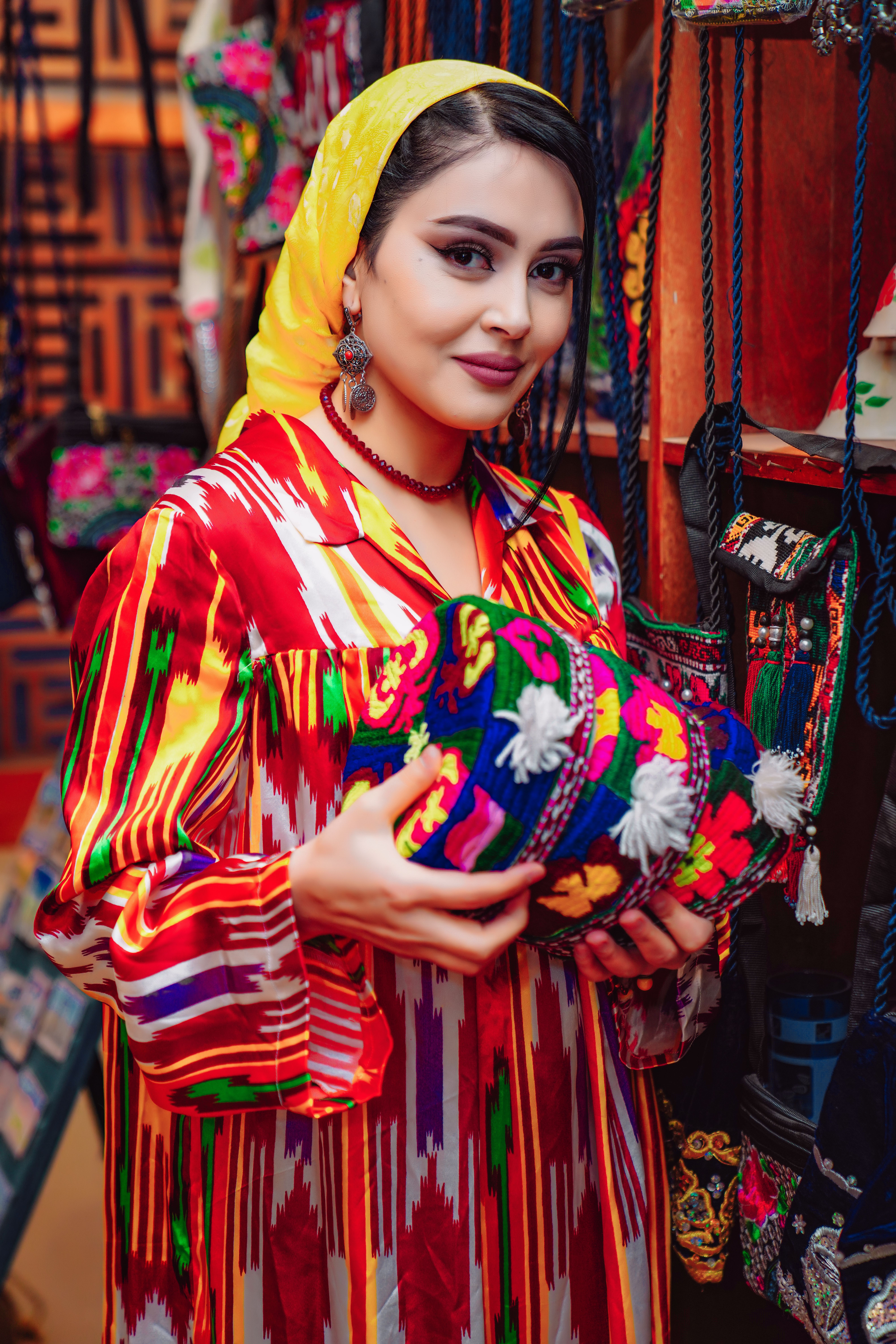 A woman in vibrant traditional attire smiles while holding a colorful handcrafted bag.