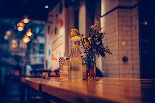 A Pitcher of Water Beside Glass Vase with Yellow Flowers on a Wooden Surface