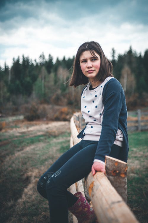 A Young Woman Sitting on a Wooden Fence while Looking Afar