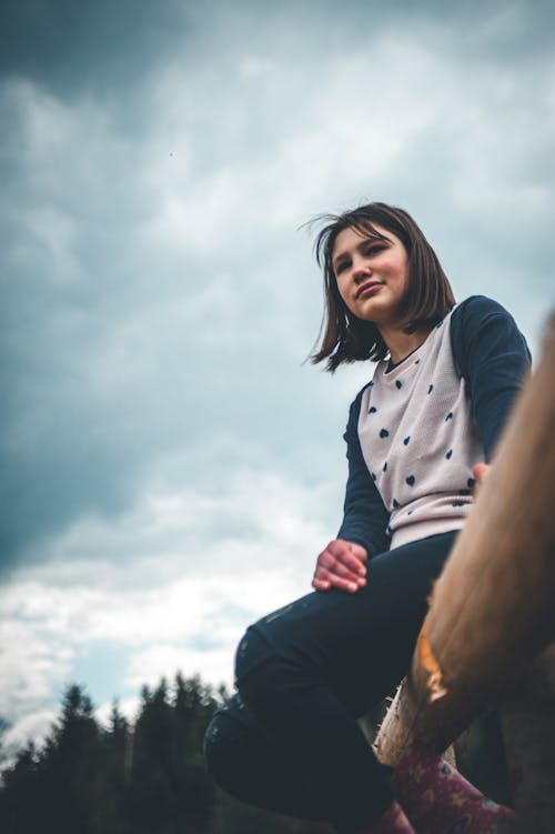 Low Angle Shot of Young Woman in Long Sleeves Sitting on a Wooden Fence while Looking Afar