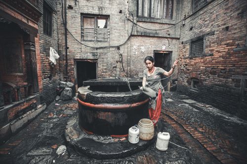Free Traditional setting with woman fetching water from a deep well in a rural courtyard. Stock Photo