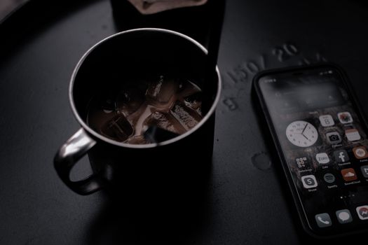 A close-up view of iced coffee in a mug next to a smartphone on a dark table.