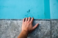 一只人手搭在水池旁的混凝土边缘，清澈的蓝色海水作为背景的特写镜头