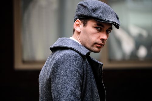 Free Portrait of a man in a gray coat and cap, looking stylish and fashionable outdoors. Stock Photo